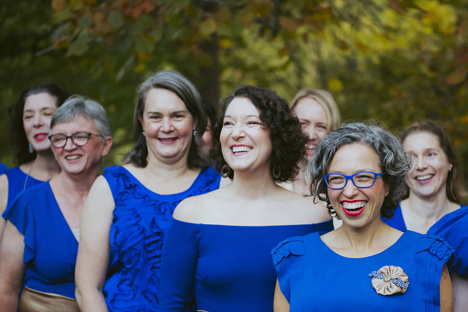 Members of the Brunswick Women's Choir dressed in blue, laughing and singing.